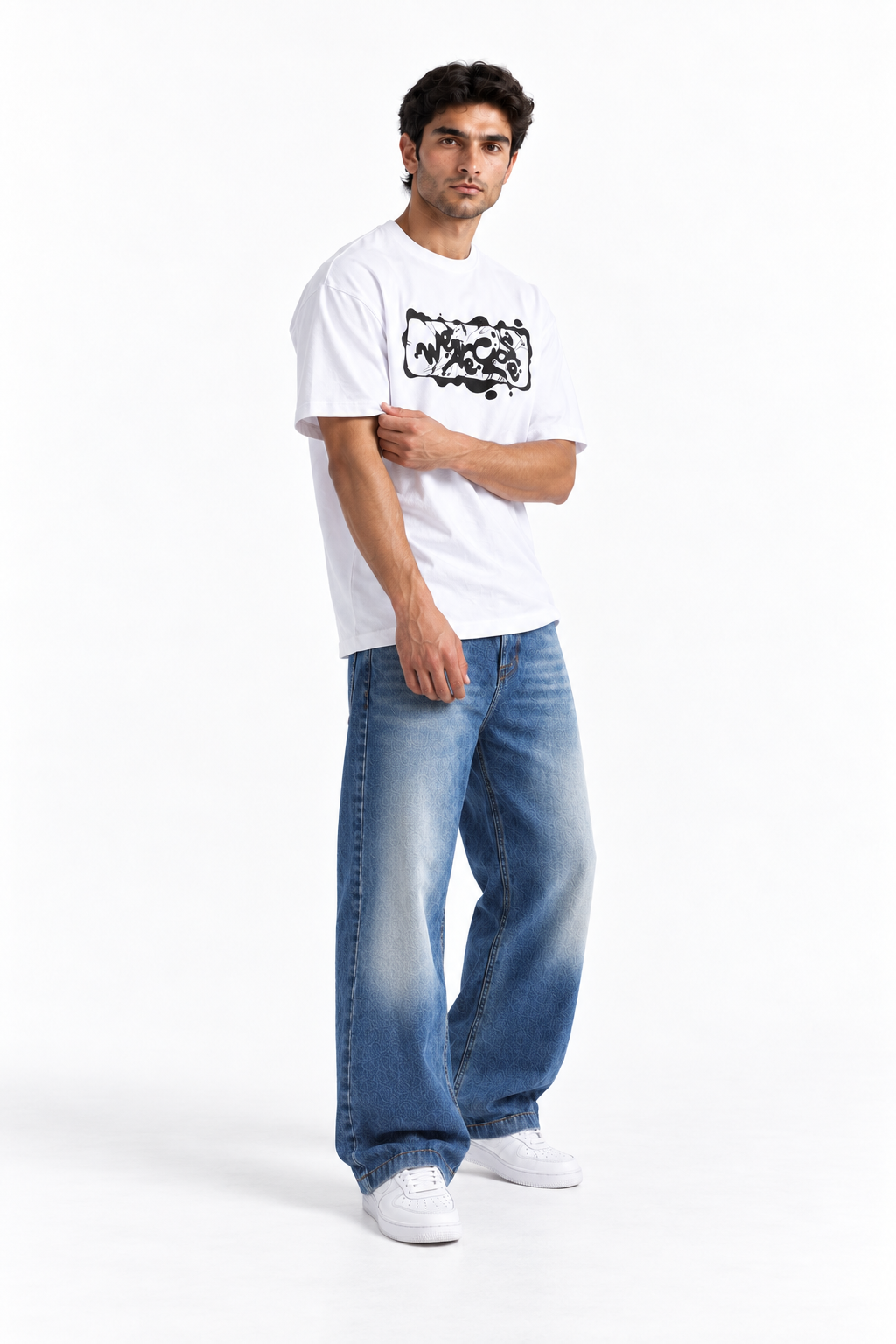 A man modeling a white short-sleeve t-shirt with a black graphic print on the chest, paired with wide-leg blue jeans and white sneakers, against a plain white studio background.