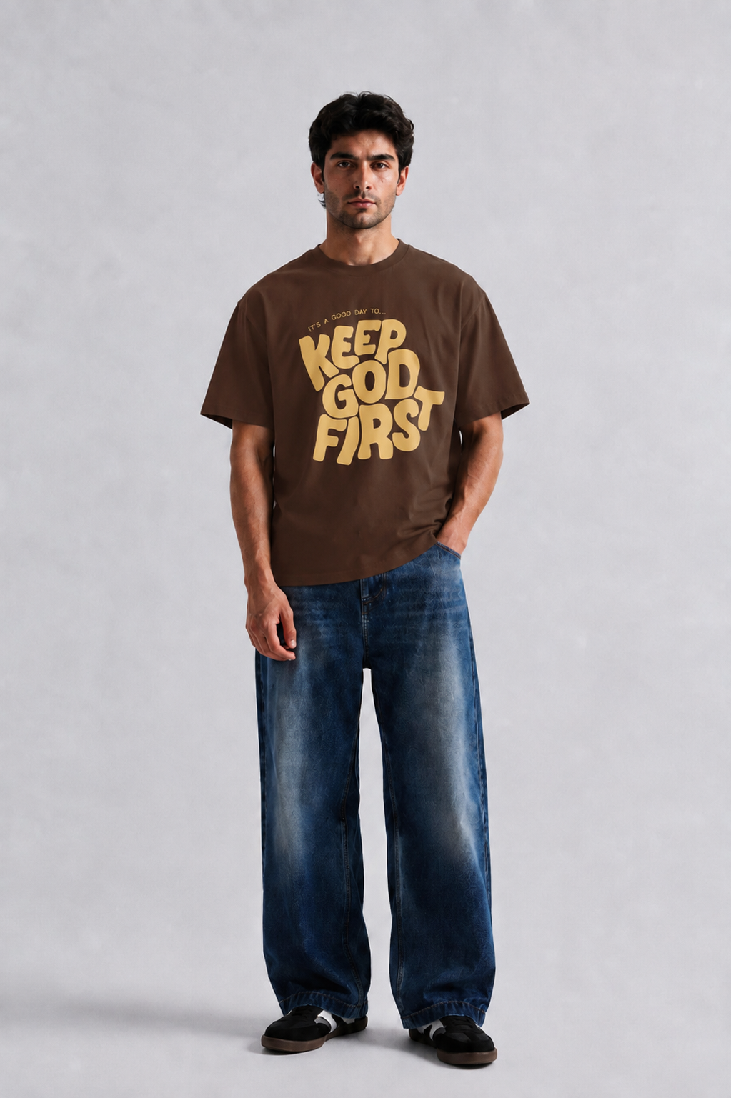 Model wearing brown oversized Keep God First graphic T-shirt with baggy blue jeans