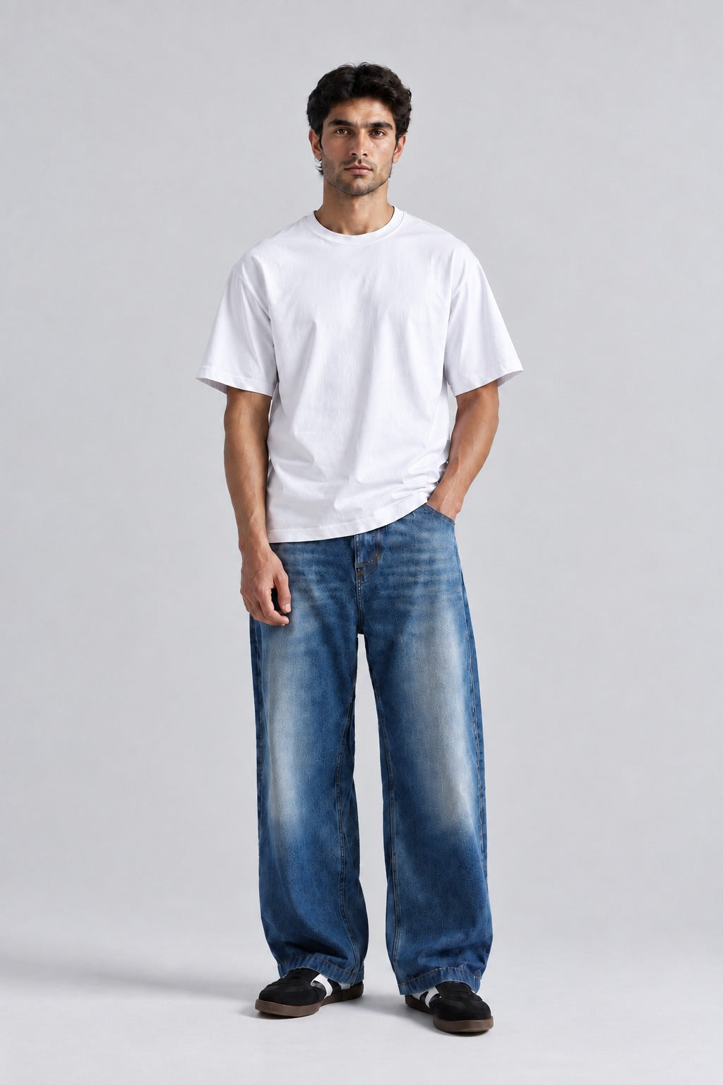 A man modeling a white short-sleeve crewneck t-shirt and wide-leg faded blue jeans, standing against a light gray studio background.